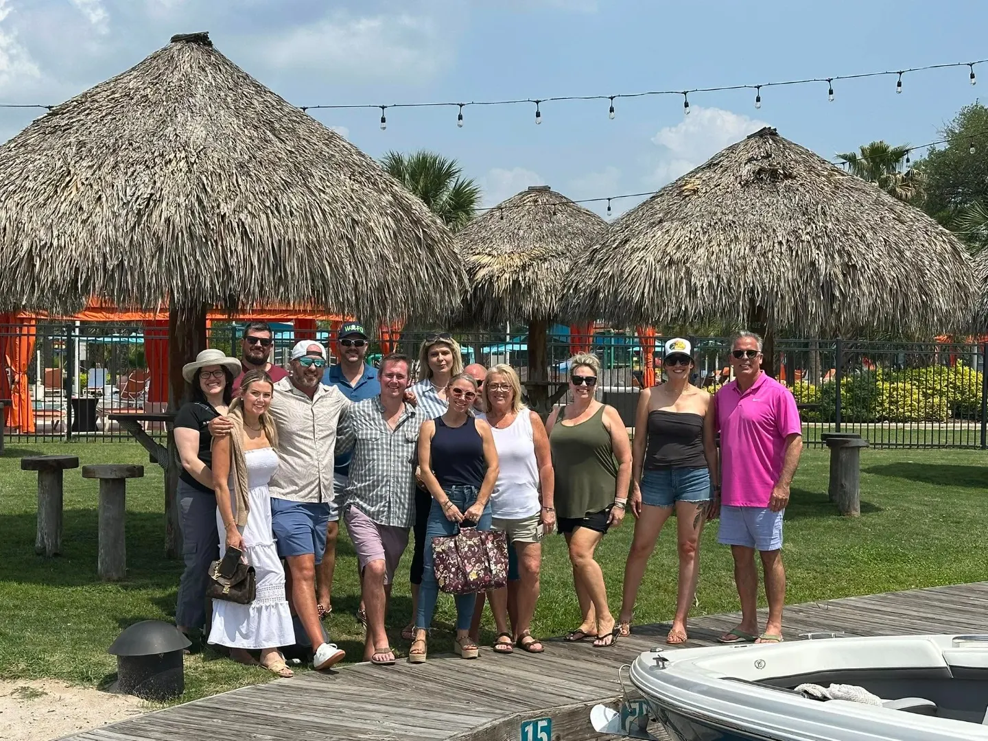 Members posing together outdoors on a sunny dock beside a lake